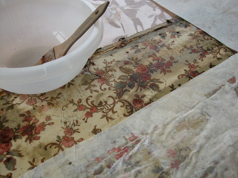 Abgedeckte Tapete mit Reinigungsmittel in Schüssel und Pinsel