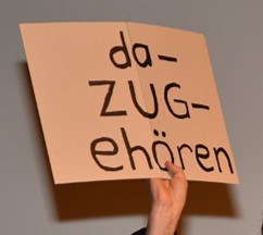 Person hält Schild mit Spruch "Da-Zug-ehören"