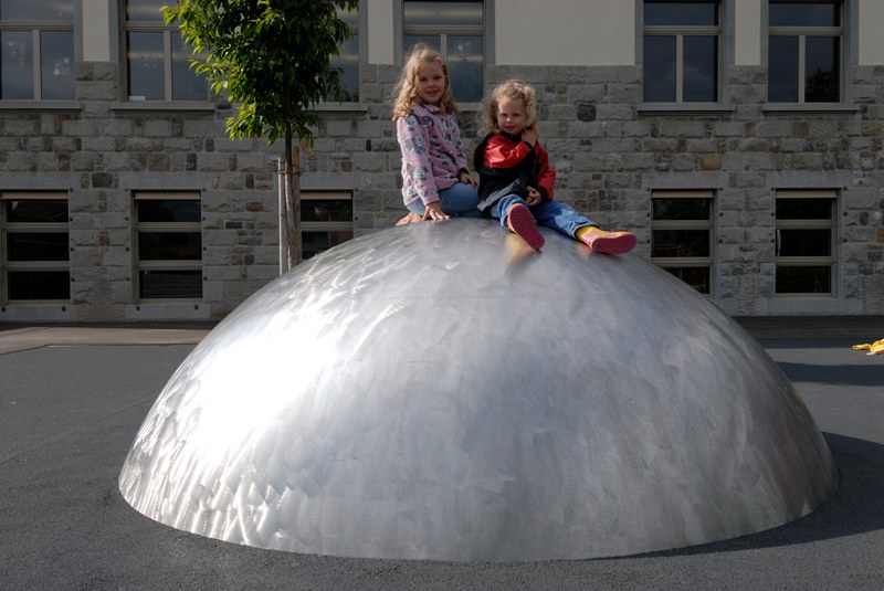 Zwei Kinder auf einer Metallhalbkugel auf dem Pausenplatz