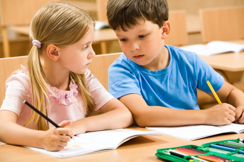 Two children are sitting on a desk and holding pens in their hands